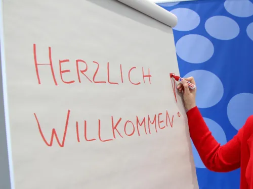 Auf ein Flipchart wird "Herzlich willkommen geschrieben"
