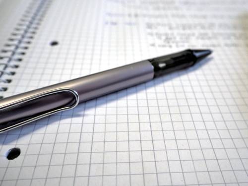 Ein Kugelschreiber liegt auf einem Schreibblock mit kariertem Papier. Handschriftliche Notizen stehen auf dem Papier.