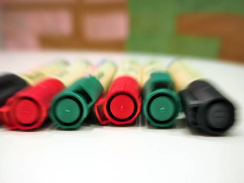 Auf einem Tisch liegen nebeneinander verschiedenfarbige Marker. Dahinter ist eine Metaplanwand, an die farbige, mit der Hand beschriebene Kärtchen geheftet sind.