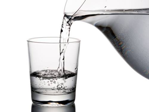 Wasser läuft aus einer Karaffe in ein Trinkglas.