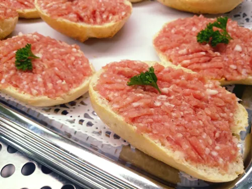 Brötchenhälften sind mit Mett bestrichen, mit Petersilie garniert und liegen auf einem Metalltablett.