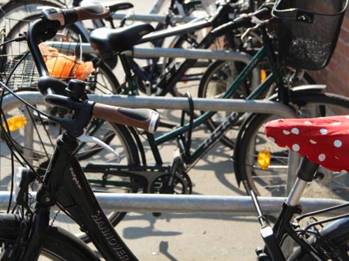 Mehrere Fahrräder, die an Fahrrädbügeln angeschlossen sind. Das Rad vorne im Bild hat einen roten Sattelüberzug mit weißen Punkten.