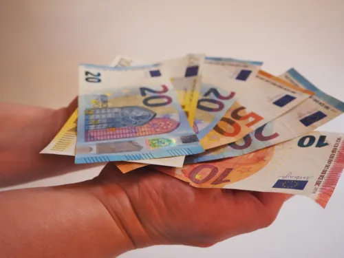 Zwei Hände tragen auf den Handflächen einen Fächer aus Geldscheinen.