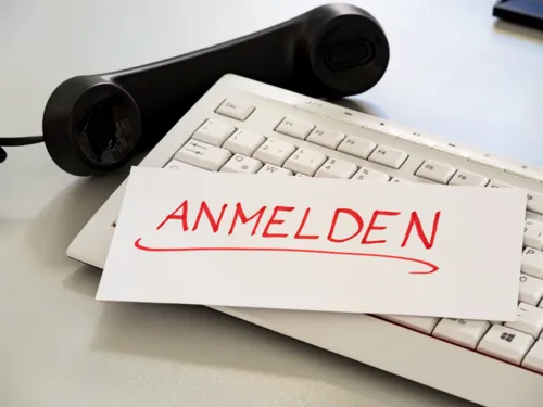 Schriftzug "Anmeldung" auf einer Tastatur, daneben liegt ein Telefonhörer
