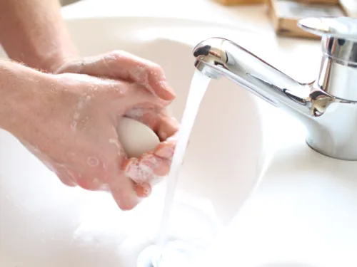 Eine Person seift sich mit einem Seifenstück neben fließendem Wasser die Hände ein.
