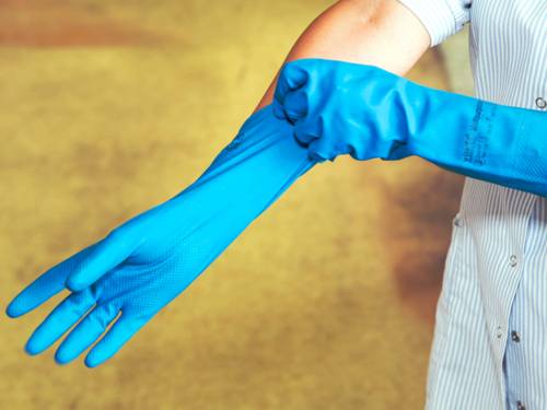 Eine Frau streift sich zwei blaue Putzhandschuhe über die Hände.