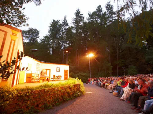 Open-Air-Bühne im Wald mit gefüllten Zuschauerreihen