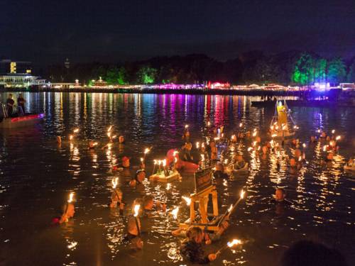 Fackelschwimmer im Wasser und die Zuschauer am Ufer.