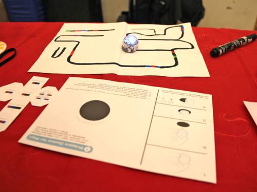 Auf einem roten Tischtuch liegt ein Spiel, bei dem eine Kugel zum Einsatz kommt (ein Ozobot).