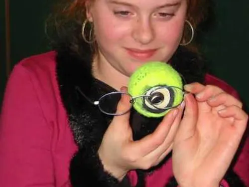 Eine Schülerin hält eine Brille vor das erstellte Augenmodell in Form eines Tennisballs