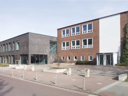 Grundschule Fichteschule: ein dreistöckiges Backsteingebäude, das von der Straße zurückgesetzt ist. Daneben der zweigeschossige Mensaanbau in dunklerem Backstein.