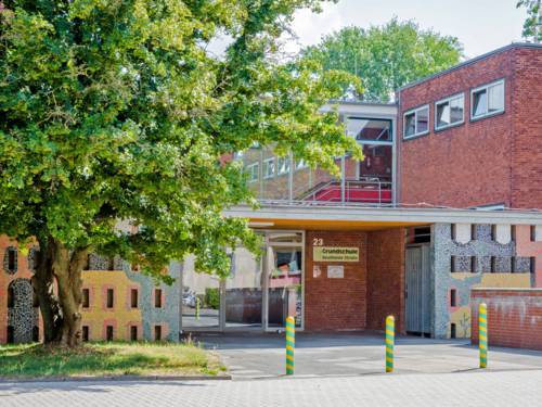 Der Eingang zur Grundschule Beuthener Straße führt in ein zweistöckiges Backsteingebäude mit Glaselementen im 1. Stock. Rechts und links ist die Fassade mit bunten Mosaiksteinen verziert