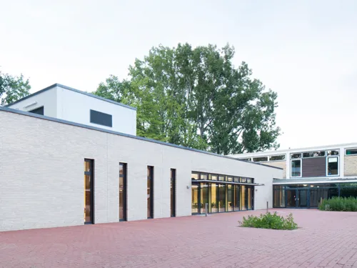 Außenaufnahme des eingeschossigen Mensa-Neubaus aus hellbeigem Klinker neben dem zweigeschössigen Bau der Wilhelm-Busch-Schule