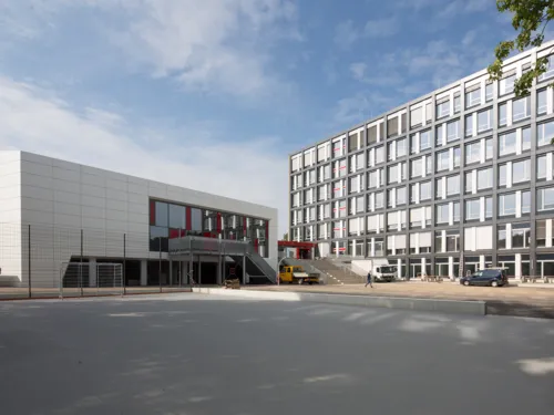 Ein siebengesch&ouml;ssiger Bau, an den sich ein breiter Treppenaufgang anschlie&szlig;t, daneben ein dreigesch&ouml;ssiger Neubau mit Au&szlig;entreppe.