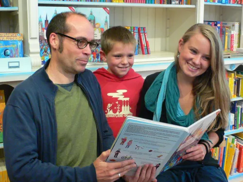 Ein Mann, ein Junge und eine Frau halten ihr Buch lächelnd in die Kamera.