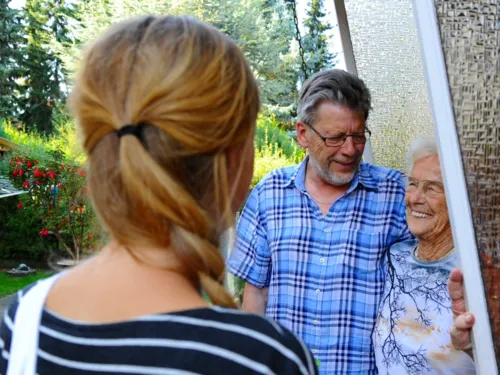 Eine jüngere Frau besucht ihre Nachbarn. Das ältere Ehepaar freut sich darüber. 
