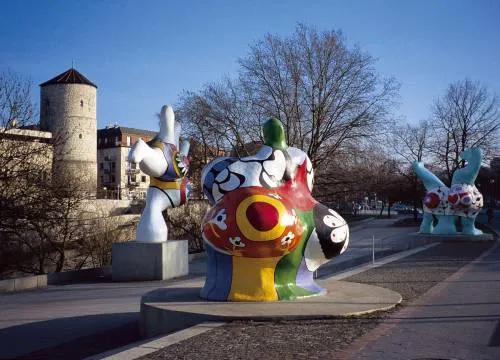Skulpturen. Im Hintergrund eine Mauer und ein Turm. 
