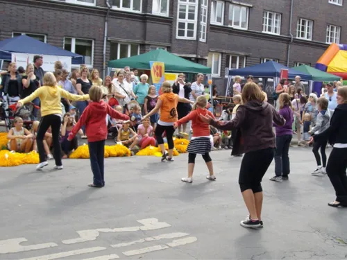 Eine Gruppe von Mädchen führt einen Tanz auf einem Stadtteilfest auf. Besucherinnen und Besucher schauen zu.