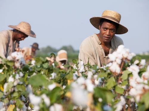 Im Bild zu sehen sind afroamerikanische Sklaven, die auf einem Baumwollfeld arbeiten.