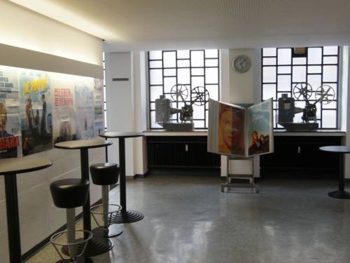 Ein Raum mit Stehtischen, Kinopostern und zwei alten Filmprojektoren.