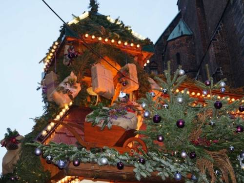 Das Dach eines Weihnachtsmarktstandes, das mit Tannenzweigen, Lichterketten, Kugeln und Präsenten geschmückt ist.