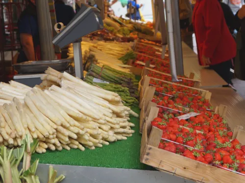Auf einem Wochenmarktstand liegen Spargelstangen (weiß und grün), Rhabarber und Erdbeeren.
