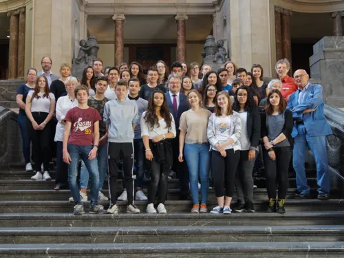 Gruppenbild auf der Rathaustreppe: Lehrkräfte sowie Schülerinnen und Schüler des St. Ursula Gynasiums und des Lycée Aristide Maillol – gemeinsam mit Prof. Dr. Carl-Hans Hauptmeyer (links oben) und Dr. h.c. Herbert Schmalstieg (rechts)