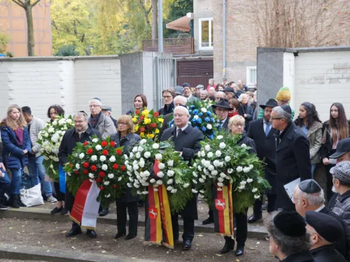 Menschen, die an einem Gedenkort Kränze niederlegen. 