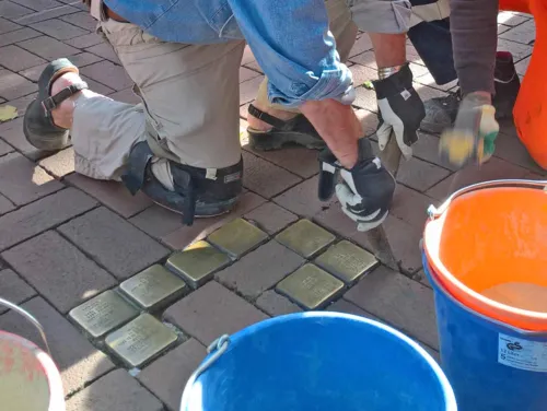 Mann, der goldfarbene Stolpersteine verlegt. 
