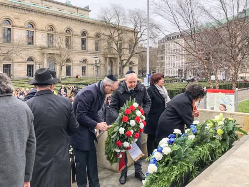 Menschen in Gedenken vor einem Mahnmal voller Blumen.