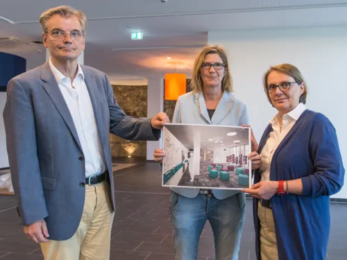 Drei Personen zeigen eine Visualisierung in einem aktuell noch recht leeren Raum