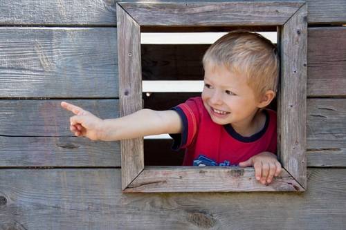 Ein Junge zeigt aus einem Holzfenster.