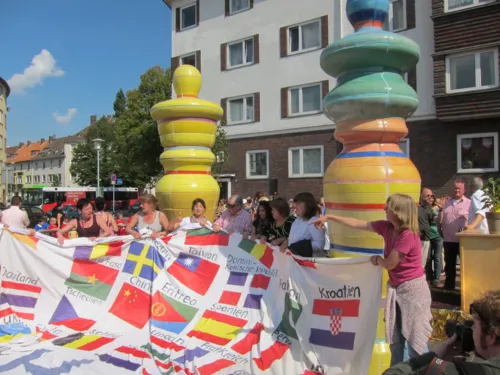 Mehrere Personen halten ein großes Banner, auf dem zahlreiche Nationalflaggen abgebildet sind.