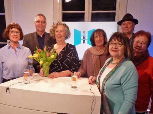 Gruppenaufnahme mit sieben Personen, die an einem Moderationstisch in einem Studio stehen; dahinter das Logo des Seniorenbeirats der Landeshauptstadt Hannover.