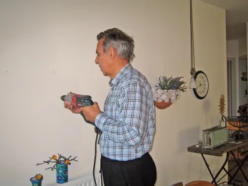Ein älterer grauhaariger Mann bohrt ein Loch in eine Wand