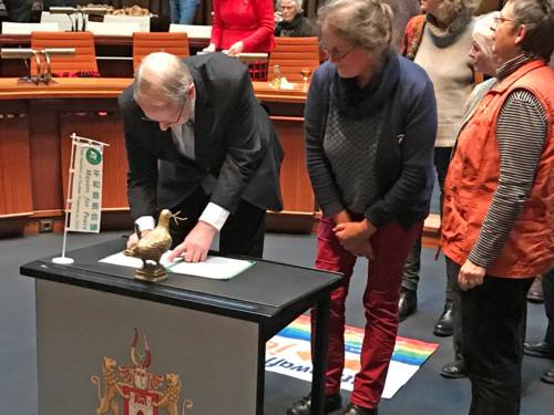 Auf einem Tisch im Hodlersaal, der mit einer Mayors-for-Peace-Fahne versehen ist, unterzeichnet der Oberbürgermeister ein Dokument.