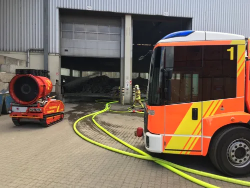 Den Brandrauch bliesen die Einsatzkräfte hierbei mit mehreren mobilen Druck-belüftungsgeräten und einem auf Ketten fahrbaren Löschunterstützungsfahrzeug über spezielle Rauchabzugseinrichtungen aus der Halle, um den Brandherd schnell und gezielt erreichen zu können. 