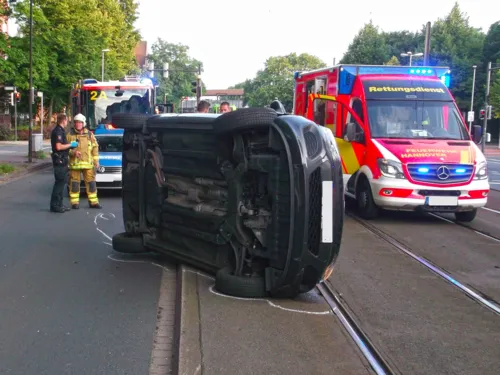 Auf der Seite liegender PKW im Bereich der Stadtbahngleise. Dahinter ein RTW der Feuerwehr Hannover mit Einsatzkräften der Feuerwehr und der Polizei.