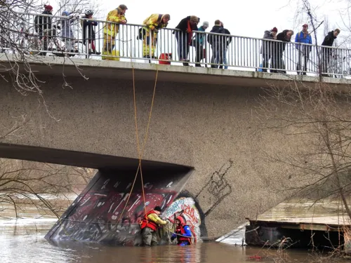 Zwei Einsatzkräfte der Feuerwehr sichern einen losgerissenen Ponton in der Lein. Sie werden durch zwei weitere Einsatzkräfte, von der oberhalb verlaufenden Dornröschenbrücke aus, gesichert.