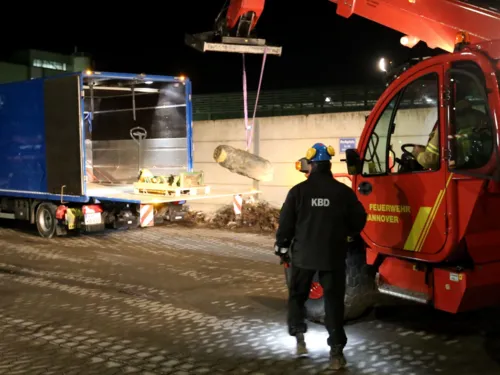 Zwei Männer, die via Kran eine Bombe abtransportieren. 