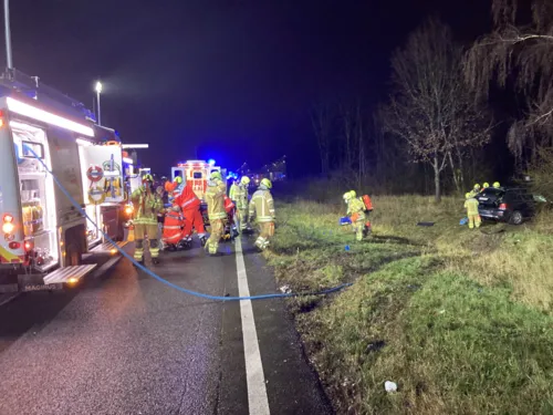 Feuerwehrautos auf der Straße und Feuerwehrleute, die einer Person helfen.