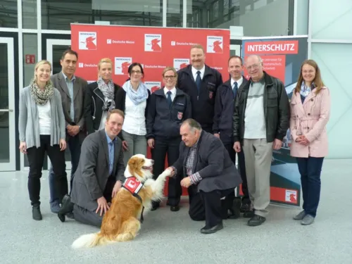 Die weltgr&ouml;&szlig;te Messe f&uuml;r Brand- und Katastrophenschutz, Rettung und Sicherheit, die INTERSCHUTZ in Hannover, hat jetzt ein eigenes Maskottchen: Rettungshund Timmy. Messe-Projektleiter Heinold und das Team von Deutscher Messe AG, vfdb und Feuerwehr Hannover begr&uuml;&szlig;en Timmy.