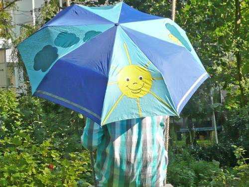 Ein Kind versteckt sich hinter einem Regenschirm, der mit einer lachenden Sonne, aber auch mit dunklen Wolken bedruckt ist.