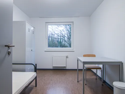 Ein Raum mit einem Bett, einem Stuhl, einem Tisch und einem Schrank