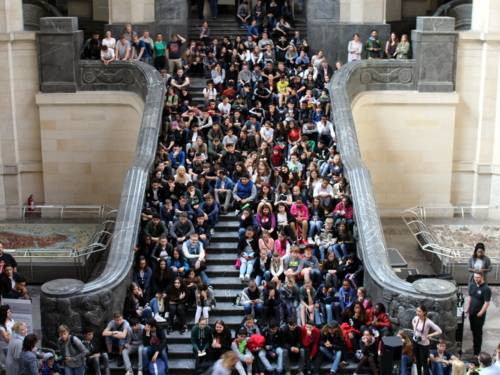 Etwa 200 Schüler/innen sitzen auf der Rathaustreppe und blicken Richtung Mitte der Kuppelhalle im Neuen Rathaus.