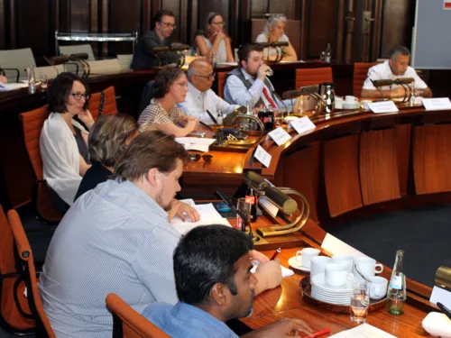 Etwa zehn Personen sitzen im Holdersaal in zwei Reihen hinter Pulten.