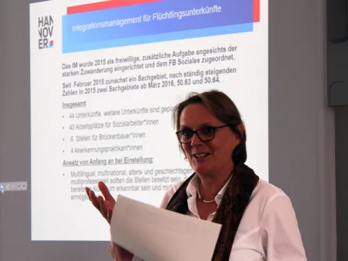 Eine Frau steht vor der Projektionsfläche eines Beamers und spricht. Auf der Projektion stehen Rahmendaten zum Integrationsmanagement.