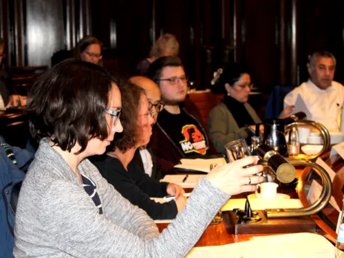Sechs Personen sitzen im Hodlersaal des Neuen Rathauses an Pulten. Einige davon blicken nach vorne, andere auf Unterlagen, die vor ihnen liegen.