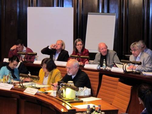 Acht Personen in zwei Sitzreihen des Hodlersaals. Die externen fünf Expert/innen sitzen in der hinteren Reihe, drei Ausschussmitglieder in der vorderen.