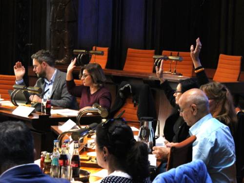 Sieben Personen - vier Frauen und drei Männer - sitzen im Hodlersaal des Neuen Rathauses hinter Pulten. Vier davon heben die Hand zur Abstimmung.